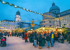 People gathered around tables at an outdoor market.  Sting lights overhead