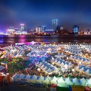 Night market with colourful lights and lots of people mingling around white tents