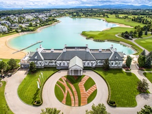 Large white golf club house surrounded by lush green golf course and a lake